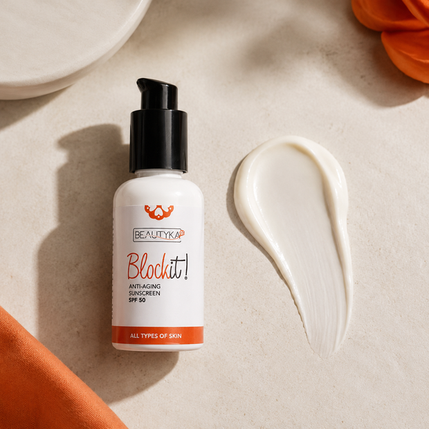 A bottle of Beautyka Block It! Anti-Aging Sunscreen SPF 50 on a textured beige surface next to a swipe of the white cream, styled with orange fabric and petals.