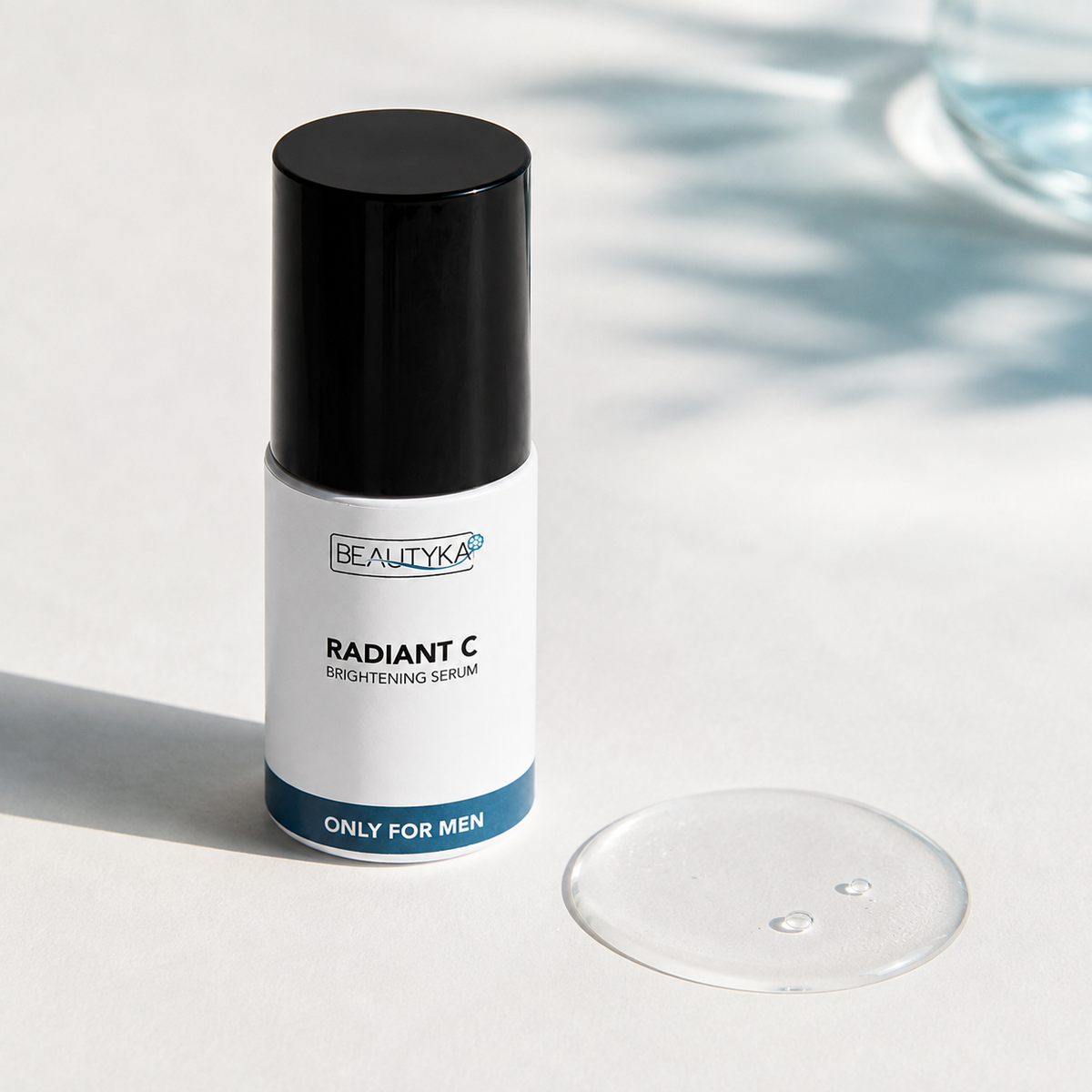 Beautyka Radiant C Brightening Serum bottle with a black cap and white label, shown on a light surface with a clear gel droplet in front.