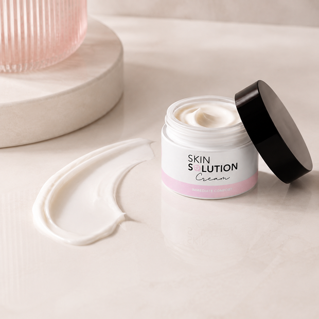 A jar of Beautyka Skin Solution Cream with its lid off and a swipe of the thick white cream on a light beige marble surface.