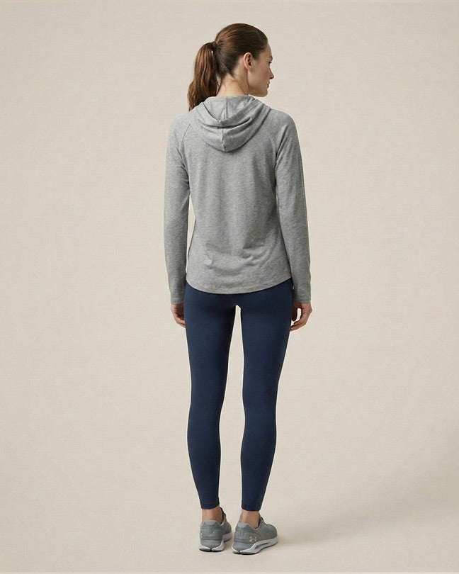 Woman in gray hooded sweatshirt and navy blue leggings, standing on neutral background