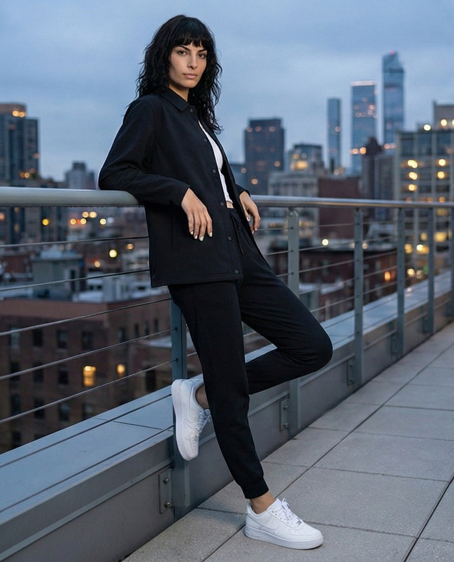 Woman in black casual outfit and white sneakers on urban rooftop at dusk
