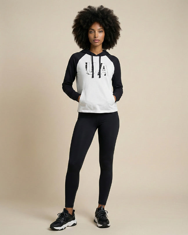 Woman in a black and white UA hoodie, black leggings, and sneakers standing indoors