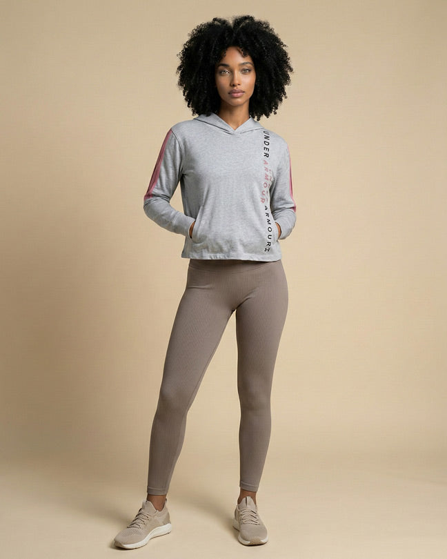 Woman wearing gray athletic hoodie with lettering, taupe ribbed leggings, and beige sneakers