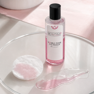 A bottle of BEAUTYKA Double Phase Eye Makeup remover sits on a clear glass tray, surrounded by a cotton pad soaked with pink liquid and a smear of the translucent pink remover, against a soft pink background.