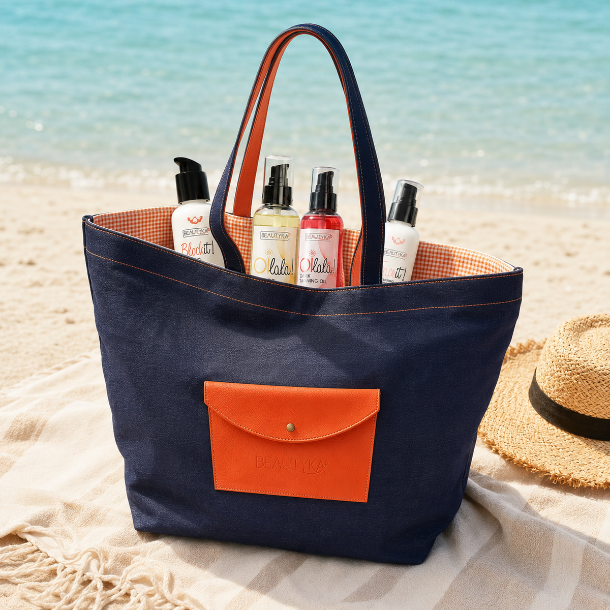 Beautyka navy and orange beach bag filled with summer skincare essentials on a Mediterranean beach.