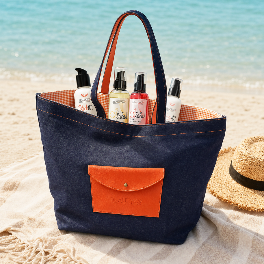 Beautyka navy and orange beach bag filled with summer skincare essentials on a Mediterranean beach.
