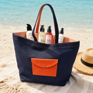 Beautyka navy and orange beach bag filled with summer skincare essentials on a Mediterranean beach.