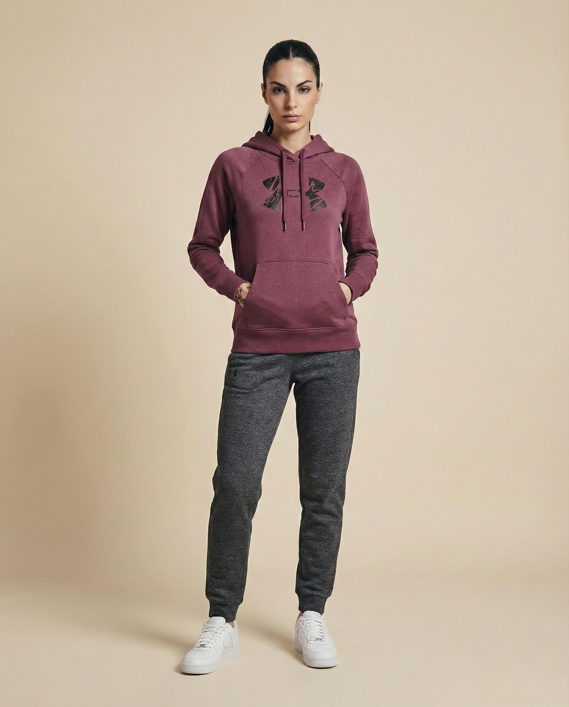 Woman wearing maroon hoodie with graphic logo, gray jogger pants, and white sneakers