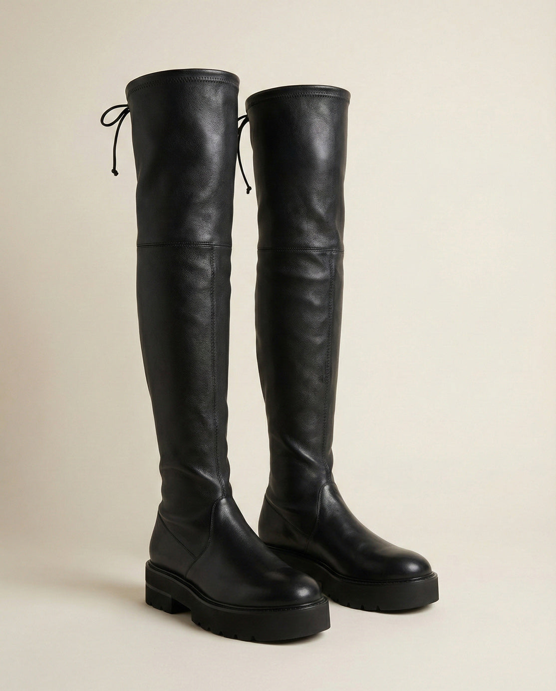 Black leather over-the-knee boots with chunky soles and lace-up detail on a neutral background