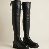 Black leather over-the-knee boots with chunky soles and lace-up detail on a neutral background