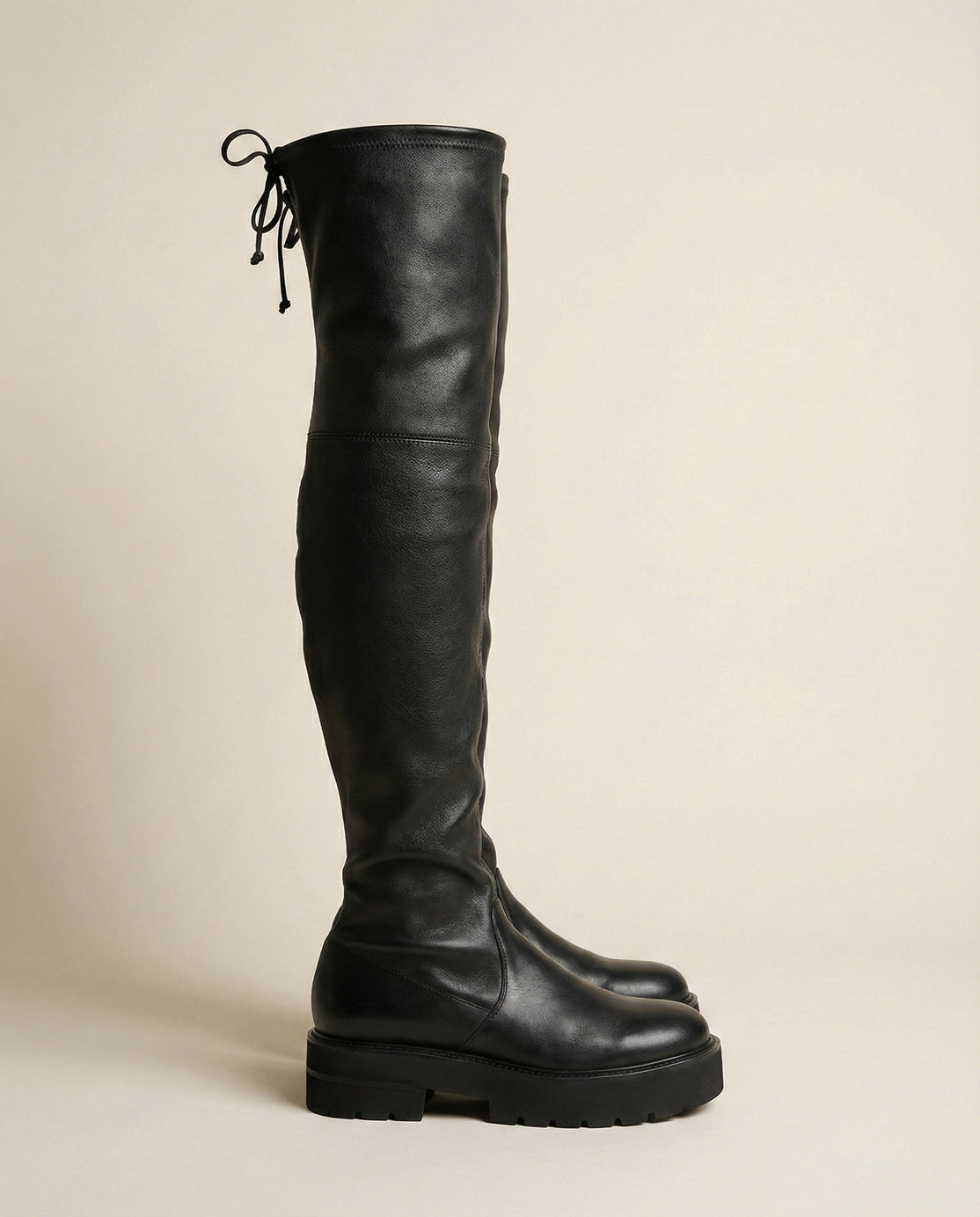 Black over-the-knee leather boot with chunky sole and back lace detail on a neutral background