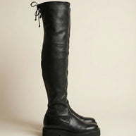 Black over-the-knee leather boot with chunky sole and back lace detail on a neutral background