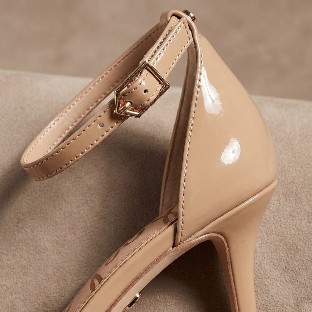 Beige patent leather high heel with ankle strap and gold buckle on neutral background