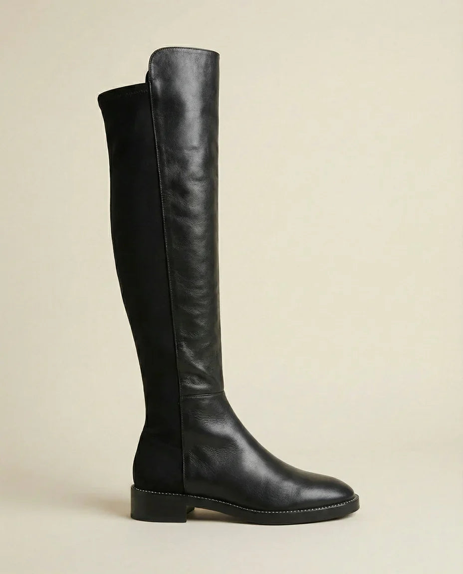Black knee-high leather boot with low heel and side stitching on neutral background