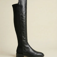 Black knee-high leather boot with low heel and side stitching on neutral background