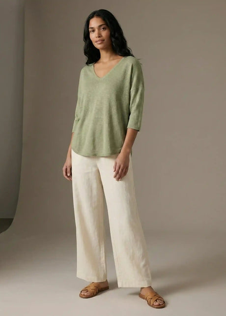 Woman modeling casual outfit with light green V-neck top, cream wide-leg pants, and sandals
