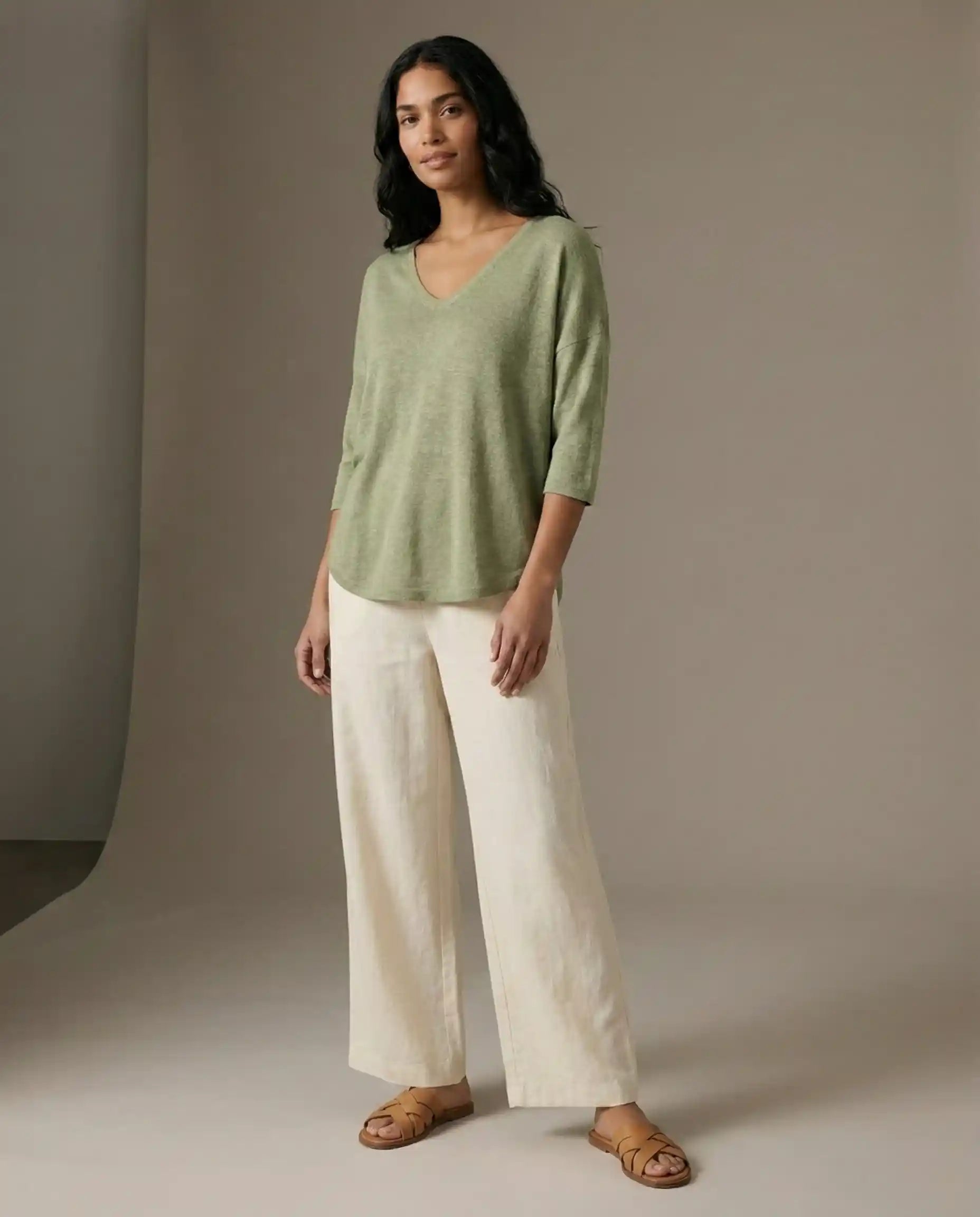 Woman modeling casual outfit with light green V-neck top, cream wide-leg pants, and sandals