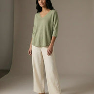 Woman modeling casual outfit with light green V-neck top, cream wide-leg pants, and sandals