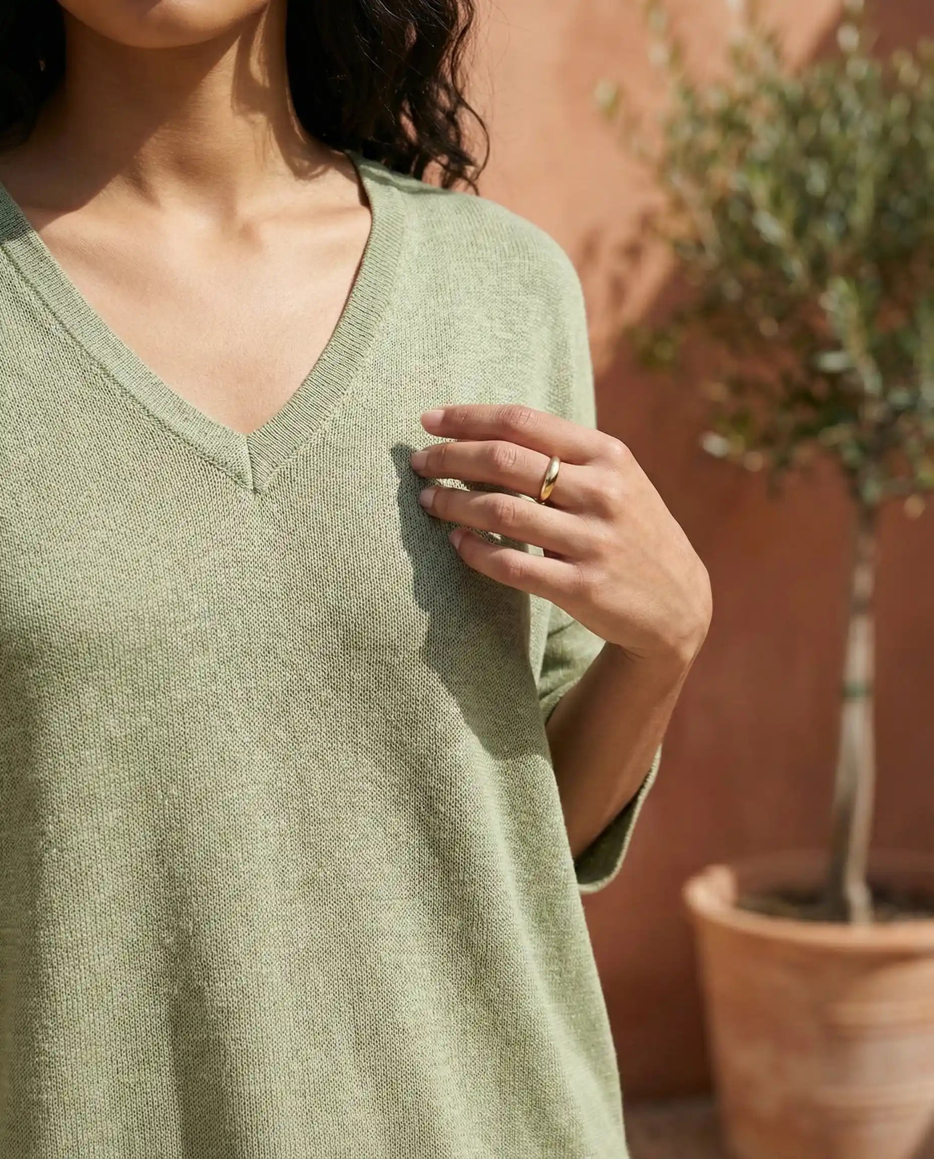 Woman wearing light green V-neck sweater outdoors with potted plant in background