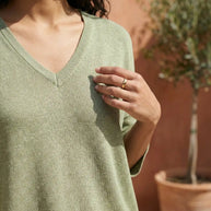 Woman wearing light green V-neck sweater outdoors with potted plant in background