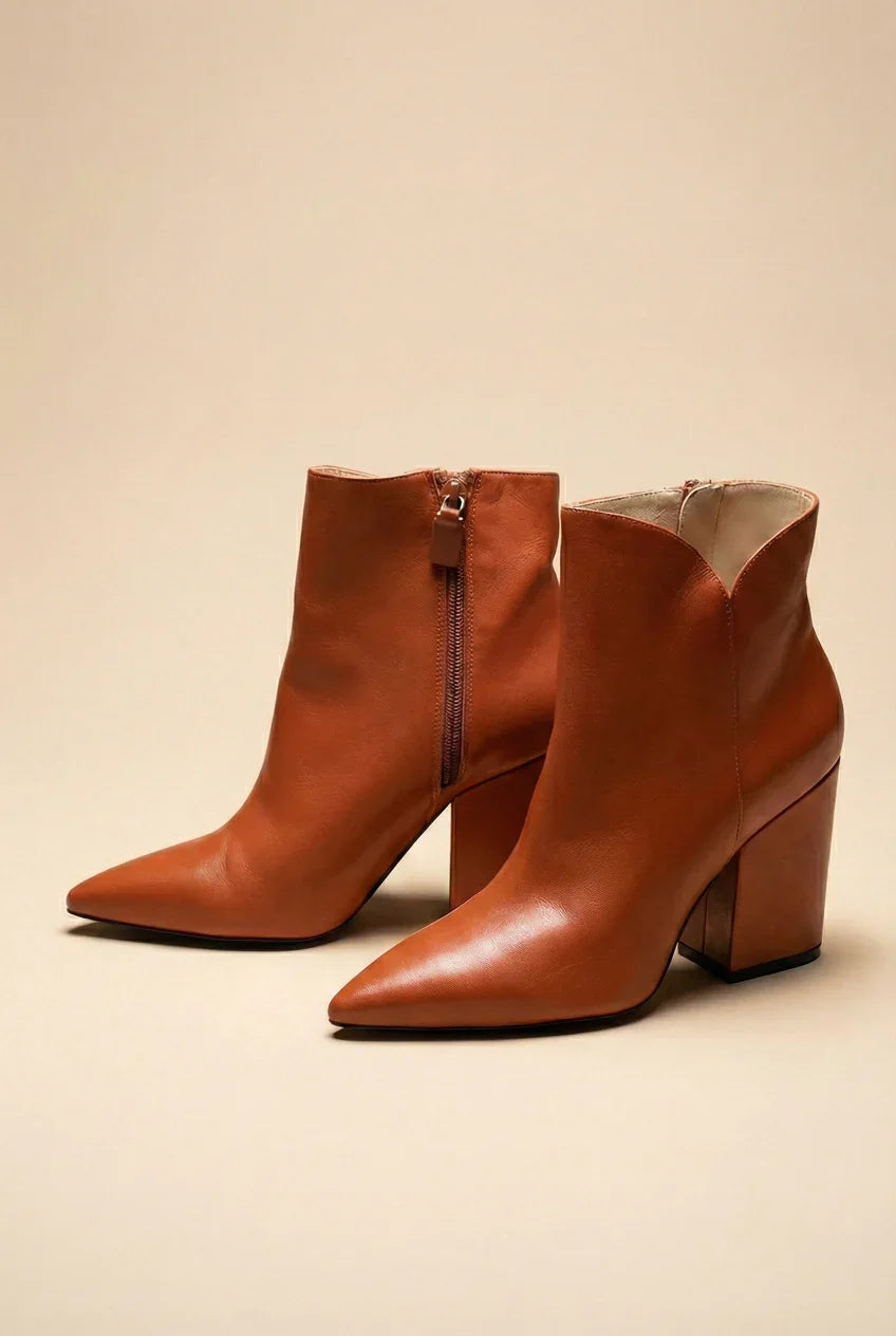 Brown leather ankle boots with pointed toes and block heels on a beige background