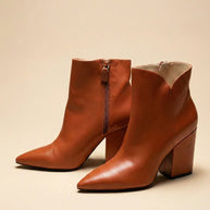 Brown leather ankle boots with pointed toes and block heels on a beige background