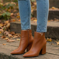 Brown leather ankle boots with block heels worn with skinny jeans outdoors on wooden steps