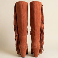 Pair of tall brown suede boots with fringe and block heels on neutral background