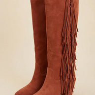 Brown suede knee-high boots with side fringe and block heel on neutral background
