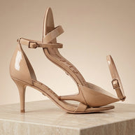 Beige patent leather ankle-strap heels with pointed toes on a marble pedestal