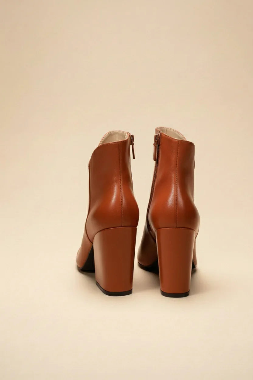 Pair of brown block heel ankle boots with side zippers on beige background