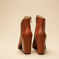 Pair of brown block heel ankle boots with side zippers on beige background