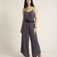 Woman in a sleeveless grey jumpsuit with spaghetti straps, black belt, and heeled sandals