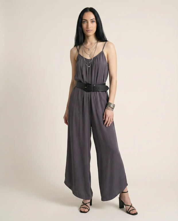 Woman in a sleeveless grey jumpsuit with spaghetti straps, black belt, and heeled sandals