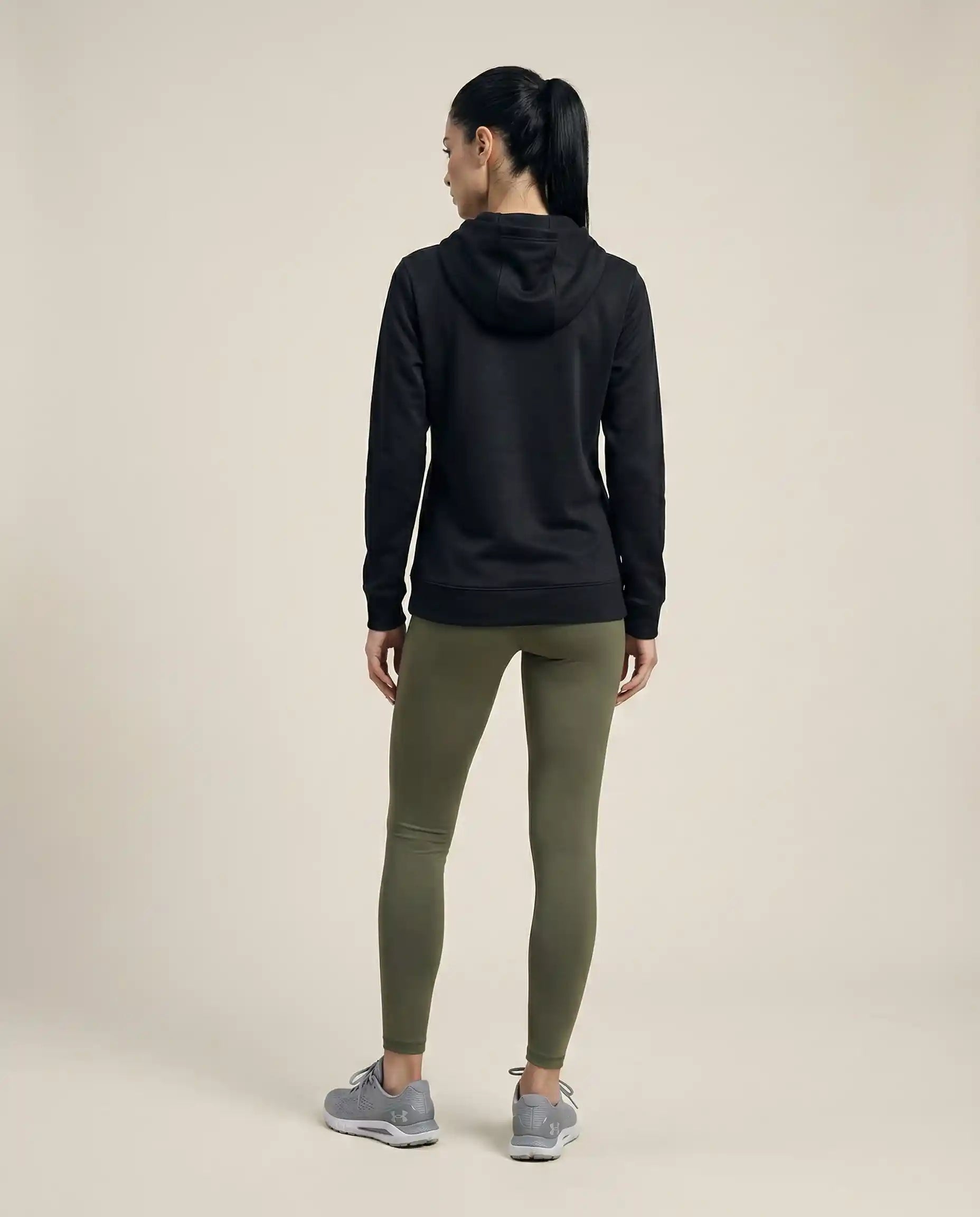 Woman wearing a black hoodie, olive green leggings, and gray sneakers, rear view