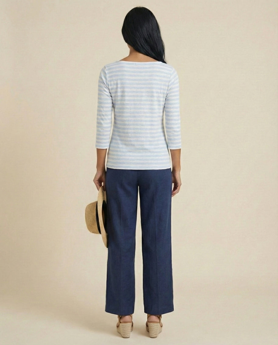 Woman in striped top and blue pants holding a straw hat, back view, neutral background