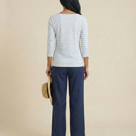 Woman in striped top and blue pants holding a straw hat, back view, neutral background