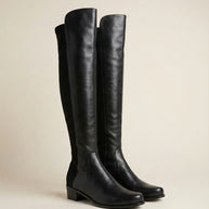 Black knee-high leather boots with low block heel on neutral background