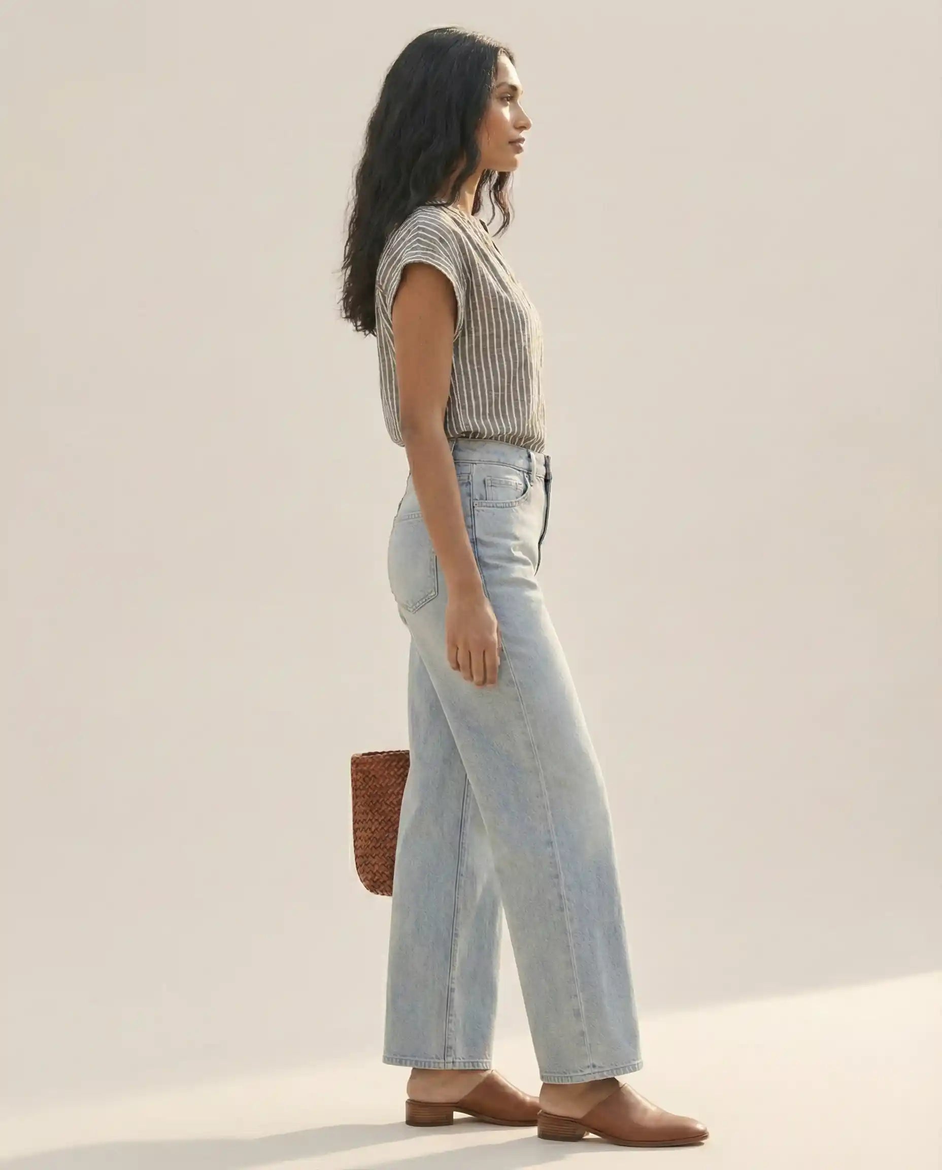 Woman modeling casual striped shirt, light blue wide-leg jeans, brown shoes, and woven bag