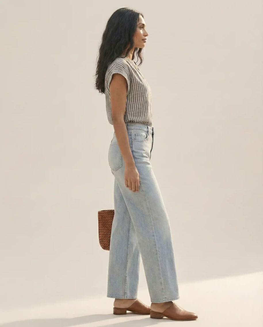 Woman modeling casual striped shirt, light blue wide-leg jeans, brown shoes, and woven bag
