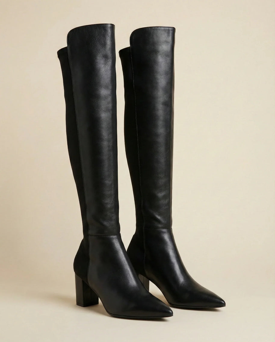 Black knee-high boots with block heels and pointed toes on a neutral background