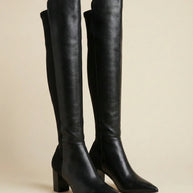 Black knee-high boots with block heels and pointed toes on a neutral background