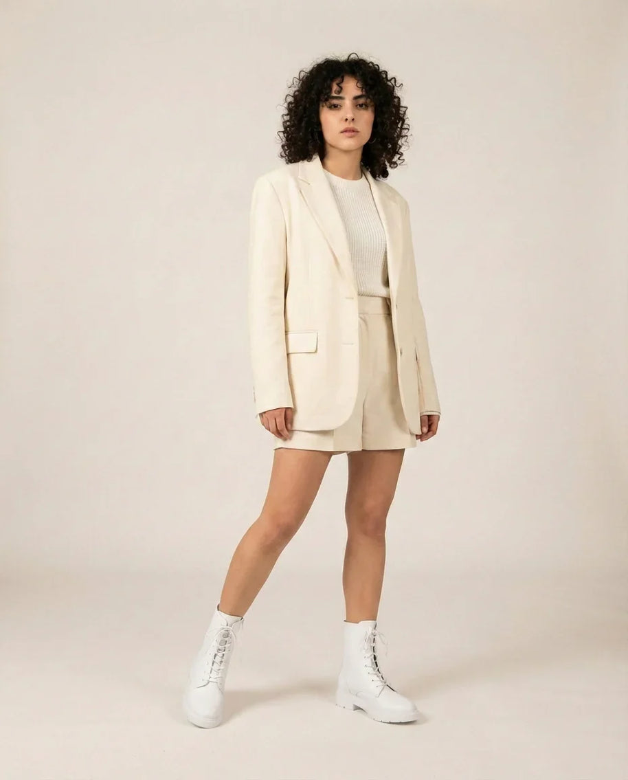 Woman in cream blazer, matching shorts, white boots on neutral background
