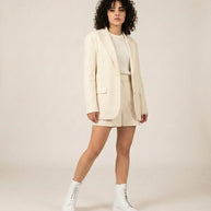 Woman in cream blazer, matching shorts, white boots on neutral background