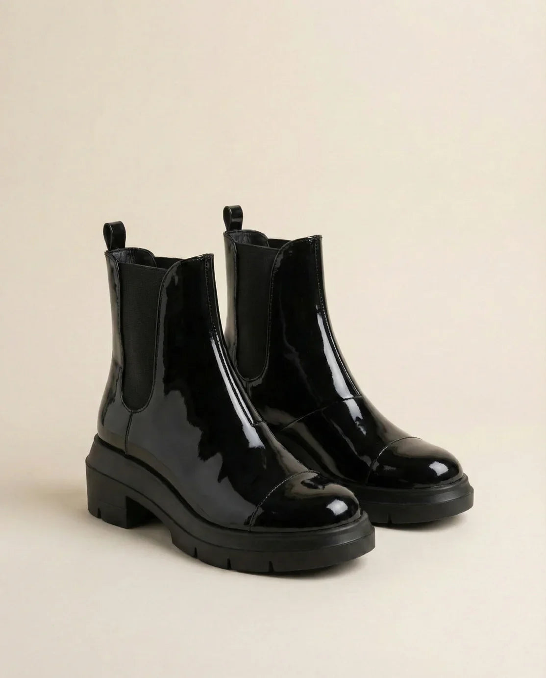 Glossy black Chelsea boots with chunky soles on a neutral background