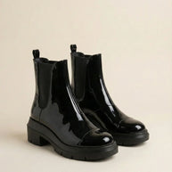 Glossy black Chelsea boots with chunky soles on a neutral background
