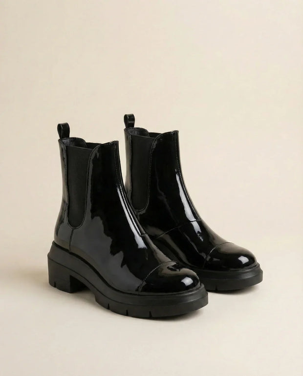 Glossy black Chelsea boots with chunky soles on a neutral background