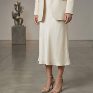 Woman in cream blazer and midi slip skirt with nude heels in art gallery setting