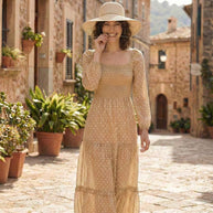 Woman in a beige polka dot dress and straw hat walking down a sunlit cobblestone street
