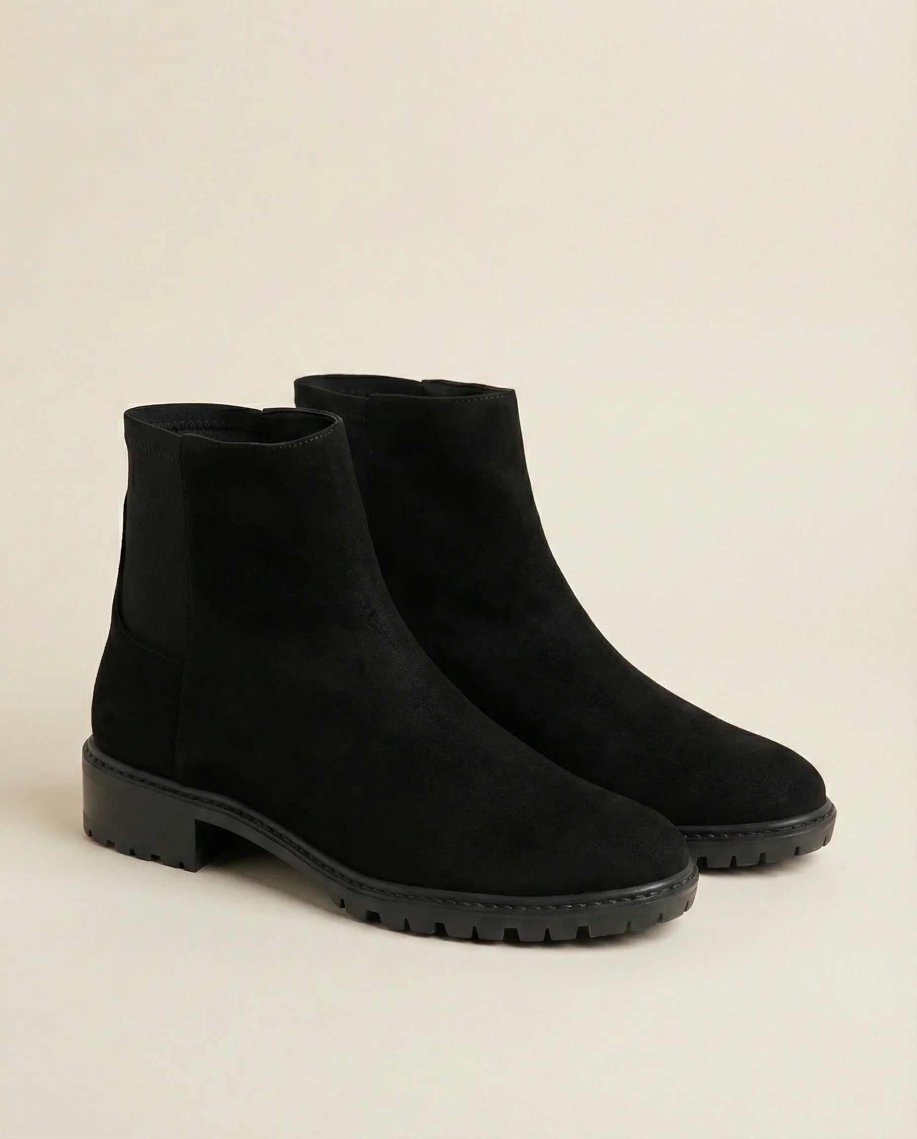 Black suede ankle boots with chunky soles on a neutral background